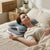 A woman relaxing on a bed with an Adjustable Ergonomic Contour Memory Foam Sleeping Pillow for optimal neck support.