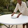 A person setting a plate on a Fold-in-Half Round Catering Table outdoors, showcasing its practical use for events.