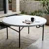 Fold-in-Half Round Catering Table with coffee mug and napkin on a patio setting.