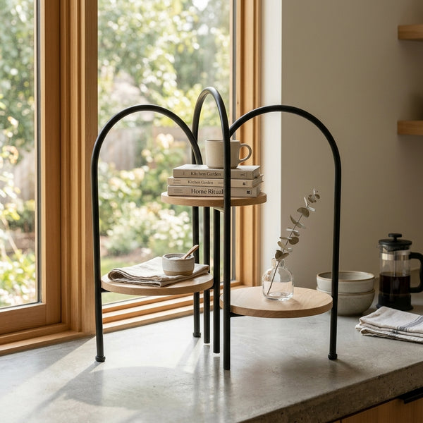 3 Tier Round Side Table with Arched Black Metal Frame displaying books and a plant near a window.