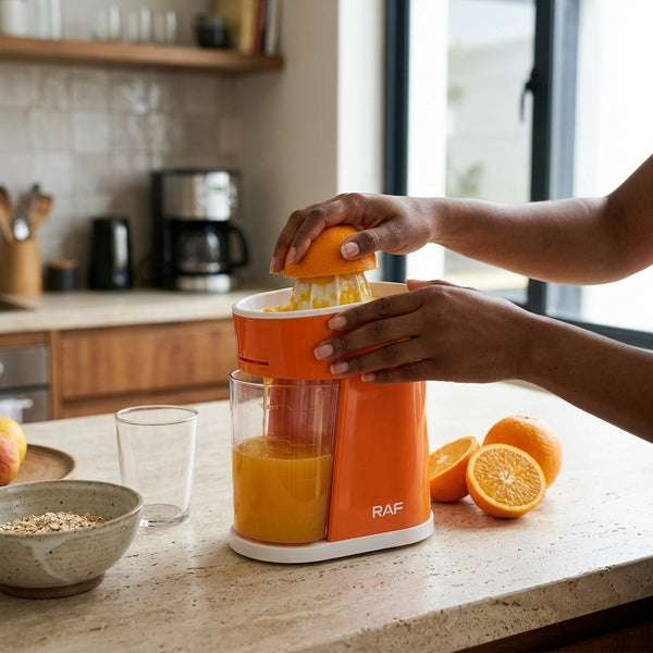 Person using Electric Citrus Juicer with 400ml Collection Cup to extract fresh juice from oranges in a kitchen.