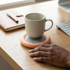 Thermostatic Heating Coaster keeping a drink warm on a wooden desk next to a notebook and keyboard.