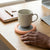 Thermostatic Heating Coaster keeping a drink warm on a wooden desk next to a notebook and keyboard.