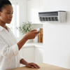 Woman adjusting settings on an Air Cooling Mist Fan remote in a modern kitchen.