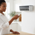 Woman adjusting settings on an Air Cooling Mist Fan remote in a modern kitchen.