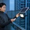 Woman adjusting a 60W Solar Floodlight powered by a solar panel on a balcony.