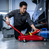 Person using a 2-Ton Manual Hydraulic Car Jack for vehicle maintenance in a workshop setting.