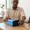Man connecting a cable to a 12V 1200W Pure Sine Wave Inverter on a wooden table with a laptop.