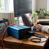 12V 1200W Pure Sine Wave Inverter connected to a laptop and battery on a workspace.
