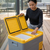 Woman using the 12-24V Portable Fridge Cooler Box 25L with its lid open, showcasing interior storage.
