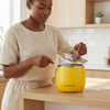 Woman using a Mini Rice Cooker in a yellow color on a wooden kitchen countertop.