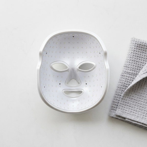 LED Face Mask – Facial LED Light Mask placed on a table next to a folded towel.