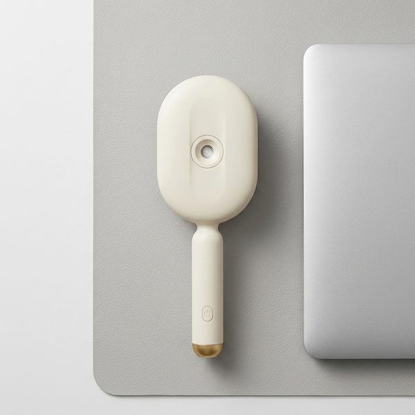 Spray Scalp Massage Comb on a desk beside a laptop, designed for gentle scalp massage and convenient spray functionality.