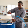 Man using a Manual Oil Transfer Pump to transfer fluid from a barrel in a workshop.