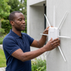 A person installing an Outdoor Wireless Access Point with External Antennas on a wall in an outdoor setting.