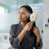 A woman using a Spray Scalp Massage Comb while wearing a bathrobe, enjoying a relaxing scalp massage in a modern bathroom.