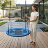 A woman stands next to a vibrant blue Hanging Saucer Swing in a modern outdoor setting, perfect for relaxation.