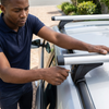 Man installing 120cm Lockable Car Roof Crossbars on a vehicle, showcasing the lockable feature for added security.