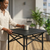 Woman placing a cup on a Folding Outdoor Table with Cross-Brace Frame on a patio.