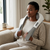 Wearable Shoulder and Neck Massager worn by a woman relaxing on a couch with a cozy outfit and a cup nearby.