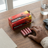 Box of 1.5V AA Batteries 40 Pack with a hand reaching for batteries on a wooden table.