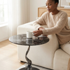 Woman enjoying coffee at a Sculptural Marble-Look Round Side Table beside a cozy sofa.