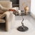 A person reaching for a cup on a Sculptural Marble-Look Round Side Table next to a cozy sofa.