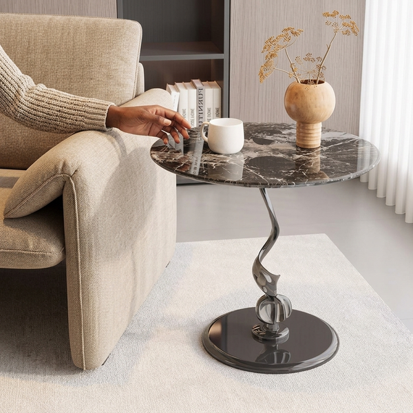 A person reaching for a cup on a Sculptural Marble-Look Round Side Table next to a cozy sofa.