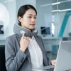 Woman using a Wearable Neck Massager while working on a laptop in a modern office setting.