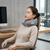 A woman relaxing with a Wearable Neck Massager while sitting at a desk, promoting comfort and hands-free relaxation.