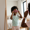 Childrens Hair Accessories & Sunglasses Set featuring a girl trying on playful pink sunglasses in front of a mirror.