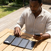 Man using a Foldable Solar Power Bank 30000mAh with 5W Panel to charge his phone outdoors.