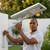 A man adjusting an 80W Solar Street Light with a solar panel outdoors in a well-lit garden setting.