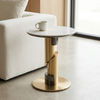 Round Pedestal Side Table beside a sofa, featuring a marble top and an elegant gold pedestal base.