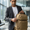 Man adjusting the Tactical Coyote Brown Rucksack in a modern indoor setting.