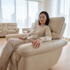 Woman relaxing on a cream-colored recliner from a 3-Piece Reclining Sofa Set in a bright living space.