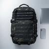 Sentinel Core Camouflage Daypack placed on a table with a laptop and smartphone.