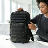 Sentinel Core Camouflage Daypack displayed by a person in an office setting, showcasing its organized compartments.