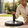 Round Outdoor Umbrella Base with Adjustable Pole Holder being set up in a garden by a person.