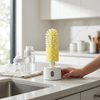 Electric Cleaning Brush with Rotating Brush Head on kitchen counter next to water bottle and baby bottle.