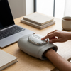 Person using a Cordless Heated Hand Massager at a desk beside a laptop and coffee.