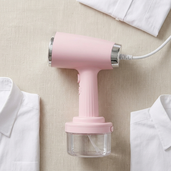 Handheld Garment Steamer with Large Capacity Water Tank next to white shirts on a beige fabric background.