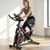 Woman using Indoor Cycling Spin Bike with Adjustable Seat in a bright home fitness environment.