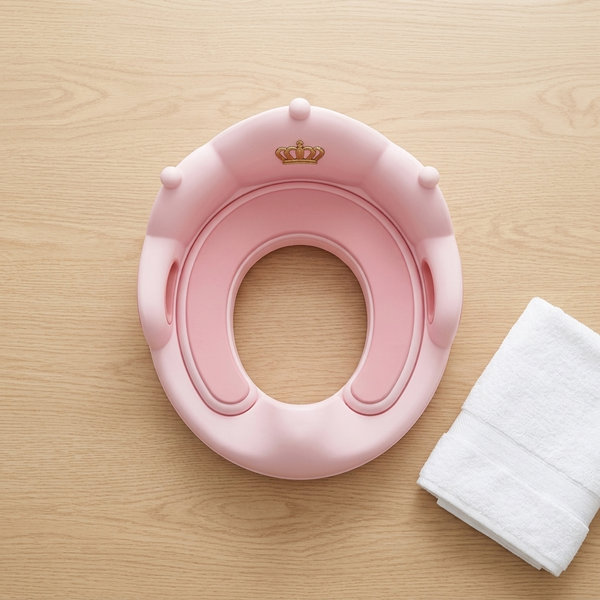 Toddler Toilet Training Seat with Handles in pink color beside a white towel on a wooden surface.