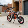 Off-Road Dirt Bike parked on a driveway with a modern home backdrop, showcasing its rugged design and knobby tires.