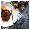 Black and Gold Stainless Steel Cutlery Set displayed with grilled steak and vegetables on a dining plate.