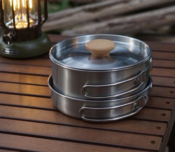 Soup Pot Pan Set of 2 stainless steel cooking pots with wooden lid on a wooden table next to a lantern.
