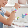 Girl wearing a colorful Slap Unicorn Bracelet while sitting at a desk with a notebook and a plush unicorn.