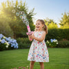 A girl joyfully using a Bubble Spray Toy in a sunny garden, creating bubbles for outdoor play.