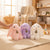Plush Bunny Toy in pink, purple, and white colors sitting on a carpet, showcasing their soft rabbit stuffed animal design.